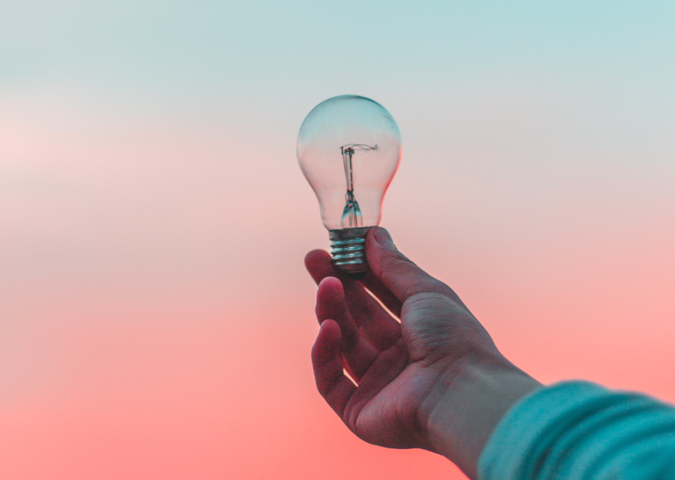 Hand holding lightbulb in front of pink and blue sunset, stay inspired despite the pandemic with discounted digital marketing services from Pepper
