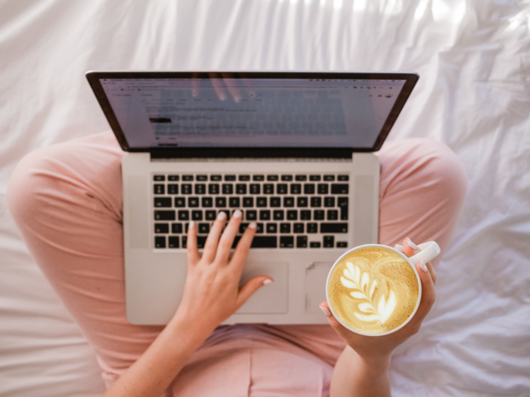woman using laptop while sitting on bed and holding a latte, discounted google ads and facebook ads for entrepreneurs