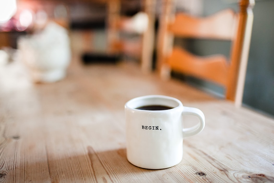 Coffee mug with word 'begin' on it sitting on a wood table, begin implemented discounted digital google ads or digital facebook ads now to help you in the future
