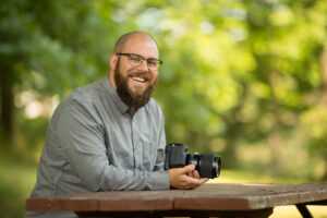 Bryan Caporicci, CEO of Sprout Social, holding a camera and smiling while sitting at a picnic table.