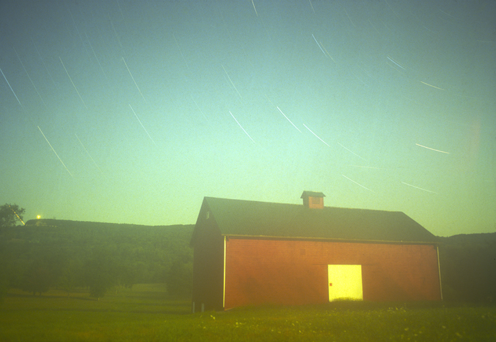 long exposure shot by jill waterman of b&h photo that shows the spin of the stars on a blue green sky behind a big red barn