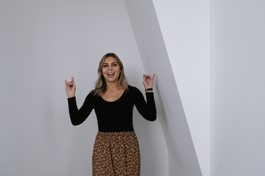 GIF of young white woman wearing black body suit and floral skirt flipping her hair and making rock n roll hand gestures because she's stoked about marketing services at pepper.