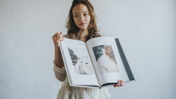Young woman in a white dress holding a large wedding photography album.