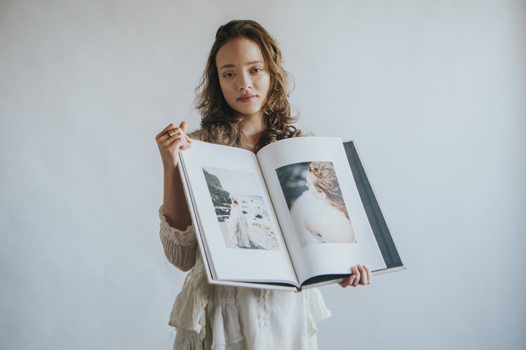 Young woman in a white dress holding a large wedding photography album.