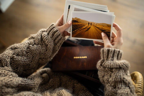 Woman with an oversized brown cardigan holding photographs of a couple and a wooden print box photography album. 
