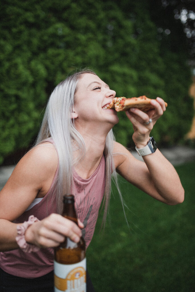 Pepper's social media expert Paris taking a bite out of a piece of pizza while holding a beer.