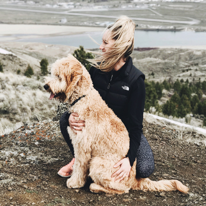 jen brown, content manager and content creator at the kamloops marketing agency Pepper, crouching at the top of a mountain with her dog.