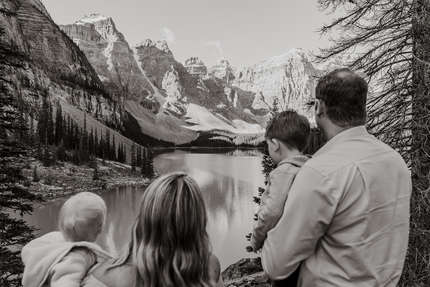 a mom and dad holding their two littles look out an alpine lake surrounded by mountains in this image from Jena Lee Photography's newsletter created by Meet Pepper's content creators. 