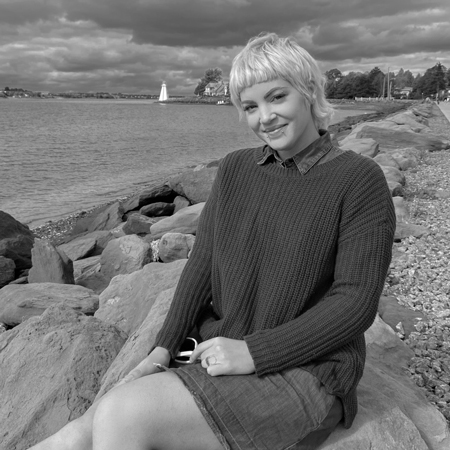 Jennifer Standing, a content creator at Meet Pepper, smiles while sitting on the rocks at the shore by the ocean.