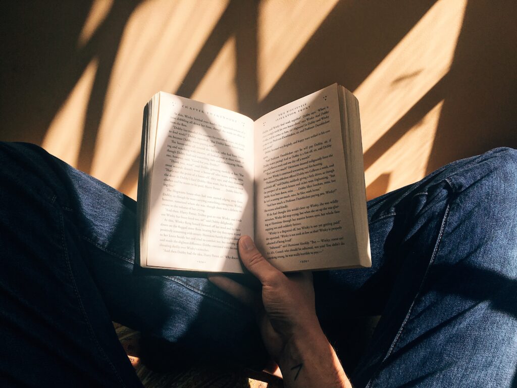 Someone sitting on the floor reading a book with sunlight creating lines on the floor from the window panes.