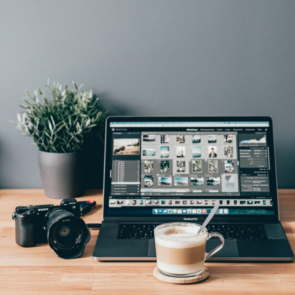 A latte and camera sitting on wood desk beside a laptop with photo editing software open for someone trying to decide on the best turnaround times for photographers.