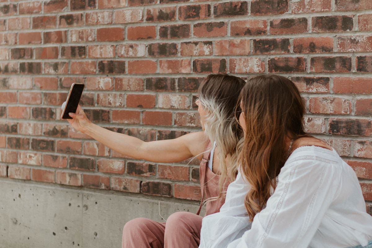 Two friends on the meet pepper team in Kamloops sitting in front of a brick wall taking a selfie to post on Instagram.