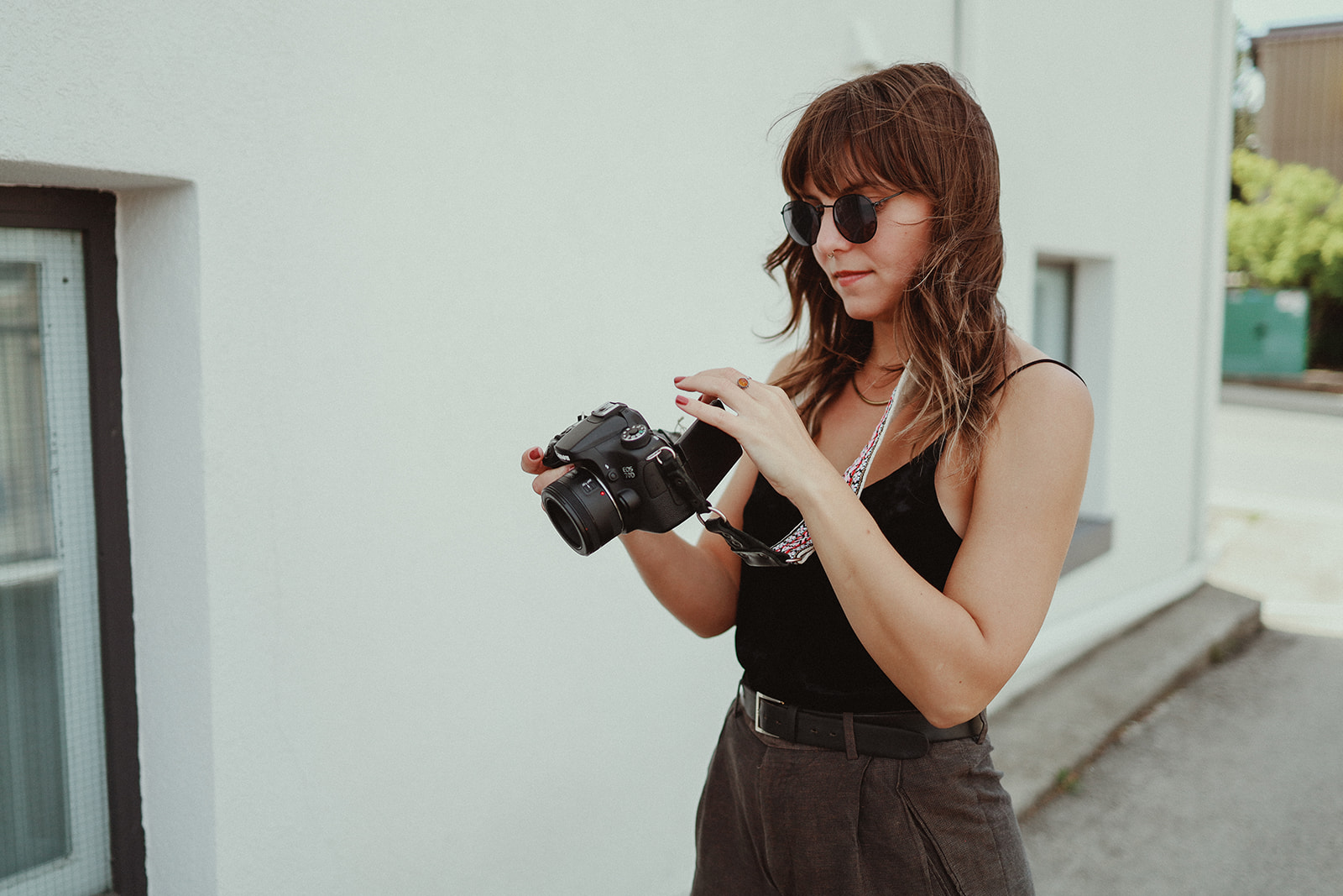 A photographer with brown hair  holding a camera looking at the photos she just took and is planning to use in a photography blog for seo to promote her business.