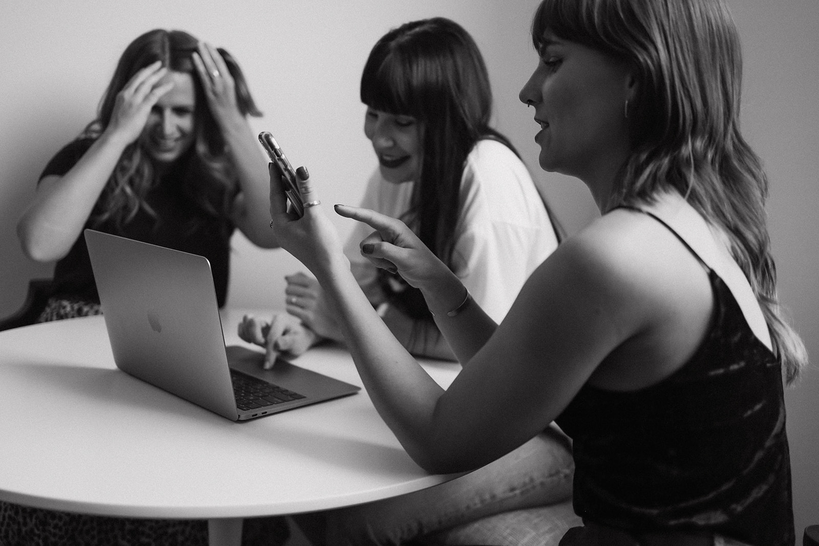 Three team members of meet pepper marketing agency sitting around a table with a laptop and cellphones looking at different marketing tactics for photographers that aren't social media.