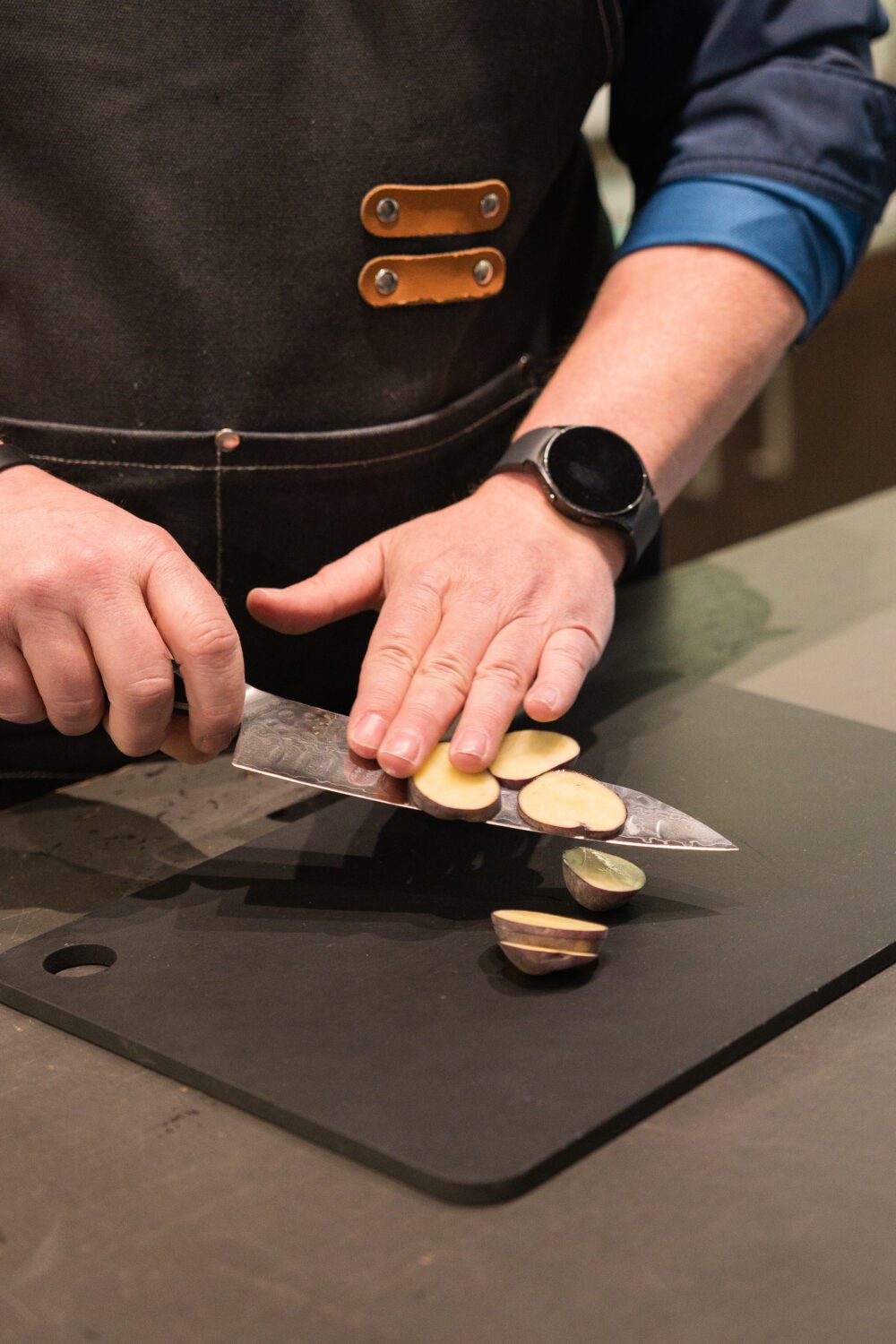 Close-up of a knife demonstration with a person slicing a small potato on a black cutting board at Aberdeen Mall.