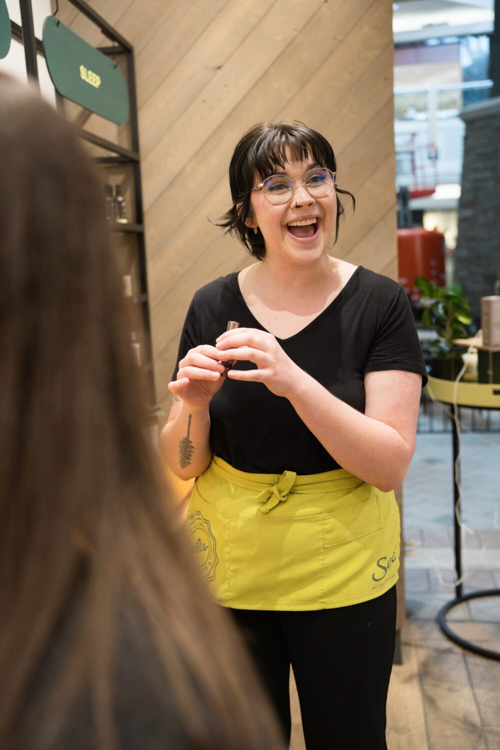 Staff member wearing a yellow apron smiling while helping a customer inside a store at Aberdeen Mall.
