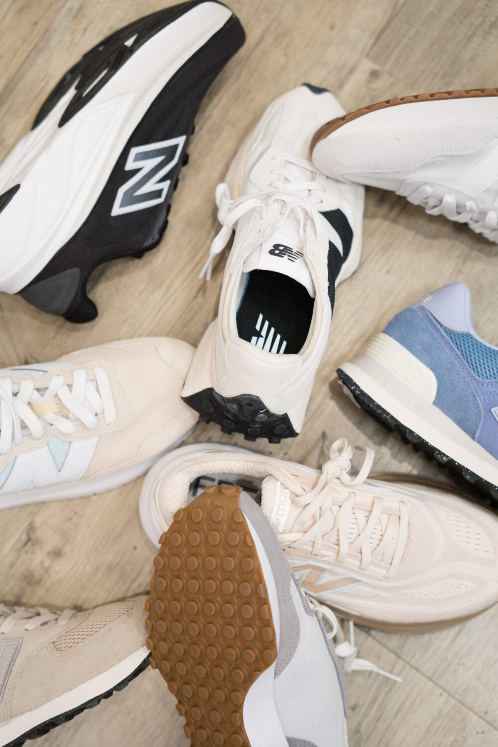 Flat lay of New Balance sneakers in neutral, black, white, and blue styles arranged on a store floor at Aberdeen Mall.