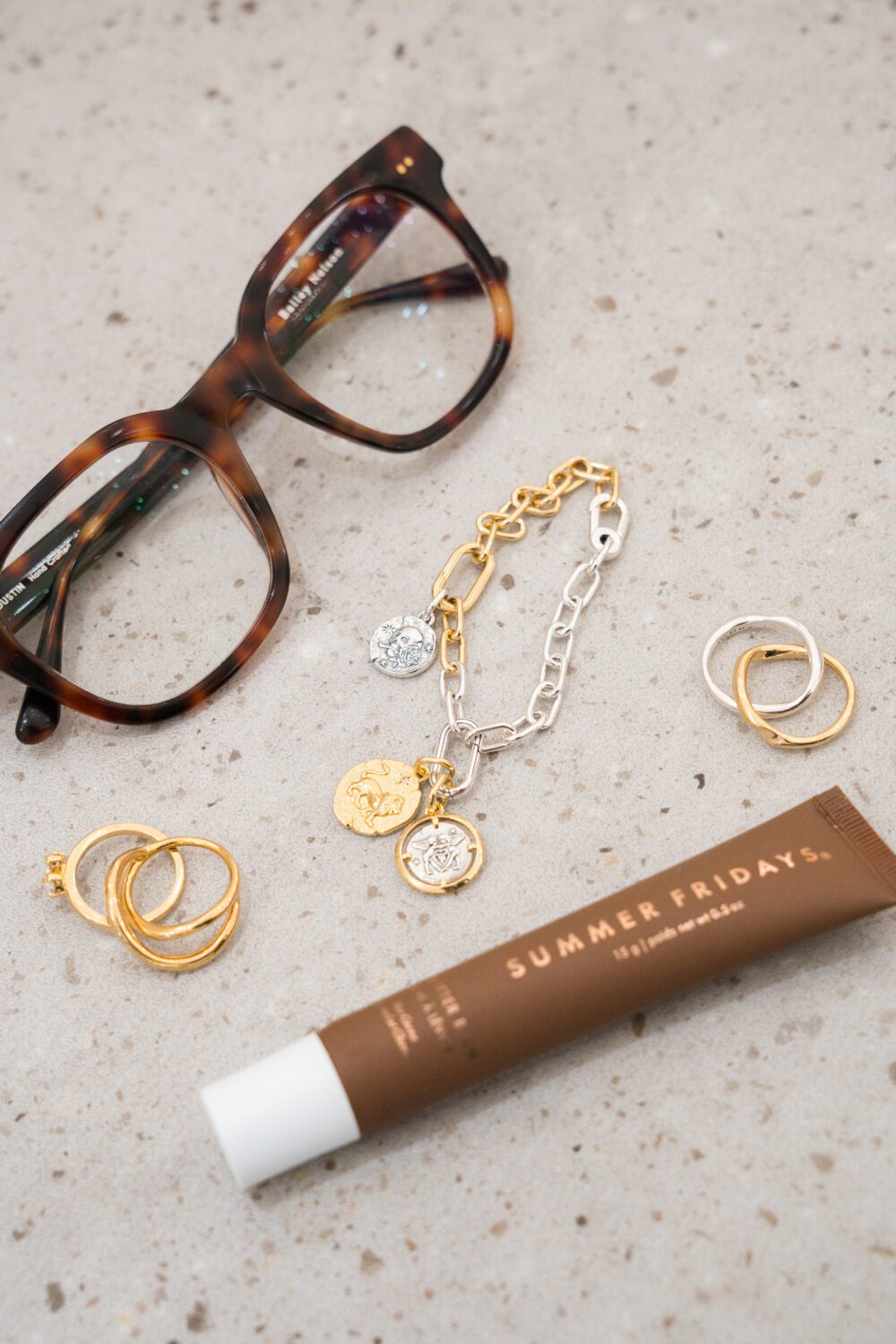 Flat lay of tortoiseshell glasses, gold and silver jewellery, and Summer Fridays lip balm on a countertop at Aberdeen Mall.