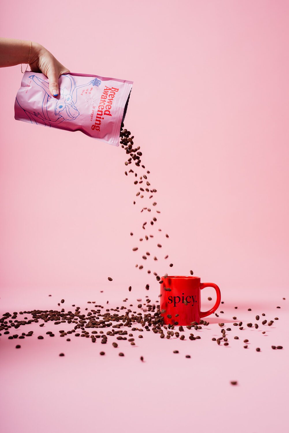 Coffee beans pouring from a pink coffee bag into a red mug on a pink background during a product photography setup used for branding, packaging promotion, and marketing visuals.