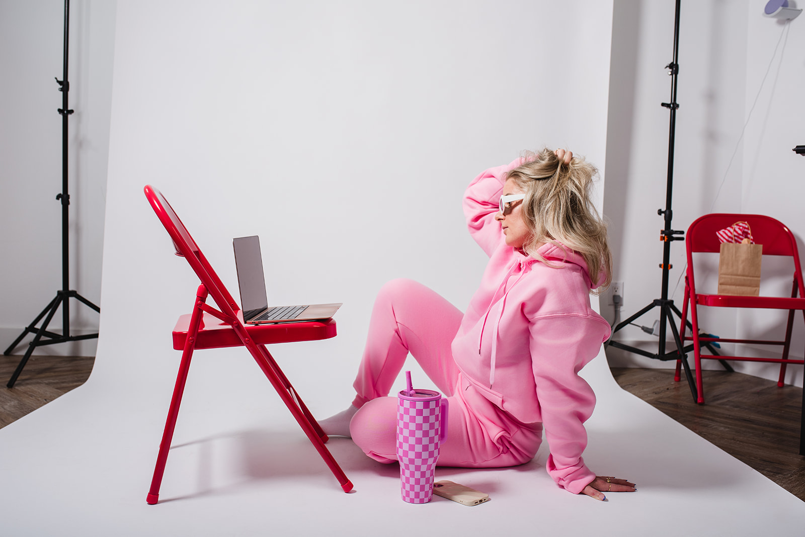 Creative team member in pink sitting on a studio floor beside a laptop and water bottle