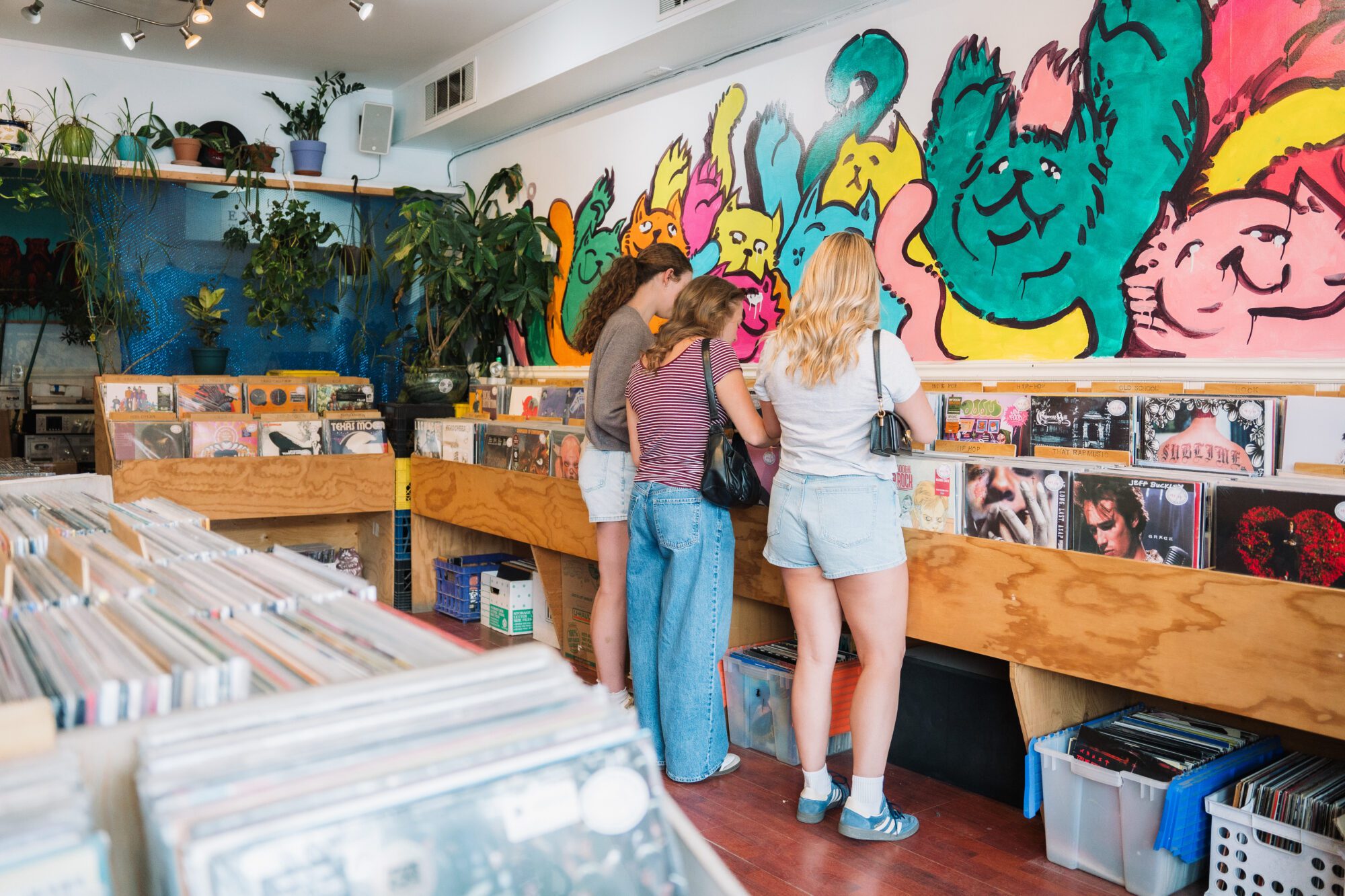 Three shoppers browse vinyl records inside Barnacle Records in downtown Kamloops, with a colourful cat mural on the wall.