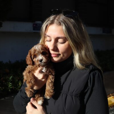 Woman holding a small brown puppy outdoors in soft natural light, creating warm lifestyle imagery often used for personal brand storytelling.