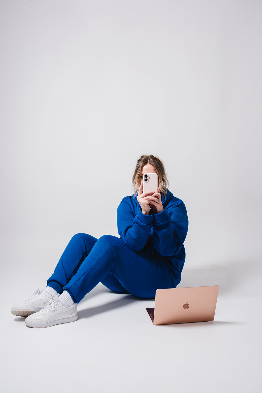 Woman in a blue outfit sitting on a studio floor beside a laptop while creating social media content