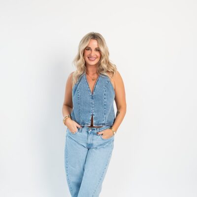 Woman in a sleeveless denim jumpsuit standing against a white studio backdrop during a lifestyle branding photoshoot for marketing and social media content.