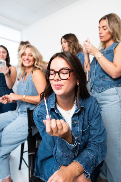 Pepper team member in foreground applying lip gloss with team in background during behind-the-scenes content shoot for marketing agency