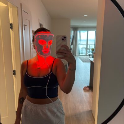 Woman taking a mirror selfie while using a red light therapy face mask at home, capturing wellness and skincare lifestyle content.