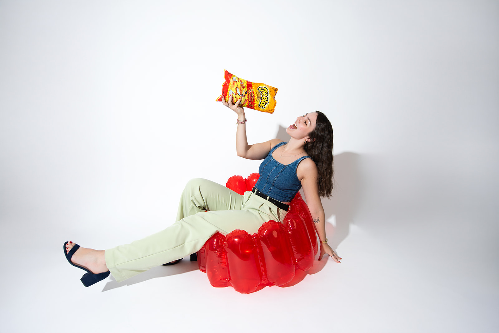 Pepper team member sitting on red inflatable chair holding snack product during playful brand photoshoot for content creation and marketing