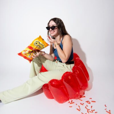 Woman sitting in a red inflatable chair eating spicy snacks during a playful lifestyle branding photoshoot designed for creative marketing visuals.