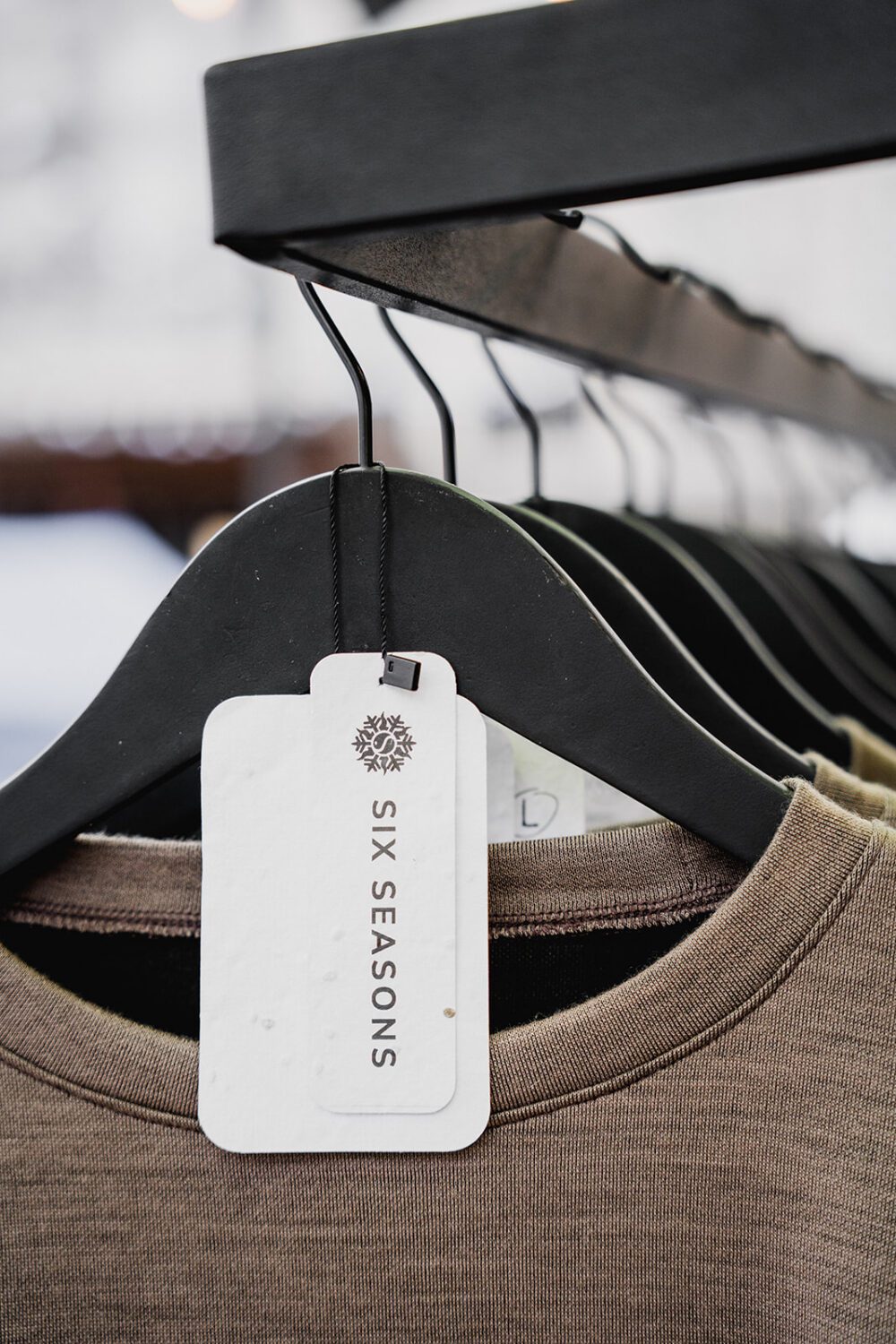 Close-up of Six Seasons apparel on black hangers with branded tag, showcasing premium retail merchandising and clean product presentation for a clothing brand.