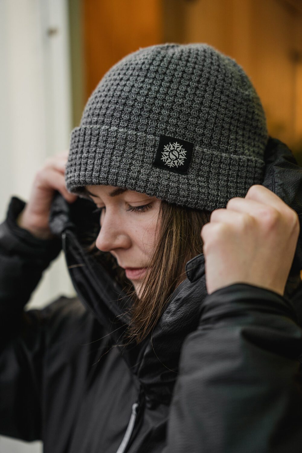 Woman wearing a Six Seasons knit beanie and jacket, adjusting her outerwear, highlighting functional, everyday apparel designed for comfort and outdoor lifestyle.