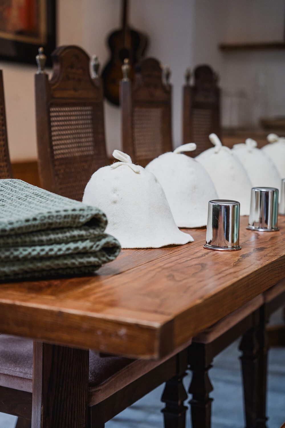 Folded green towels, felt sauna hats, and metal cups arranged on a wooden dining table inside The Spot at Paul Lake.