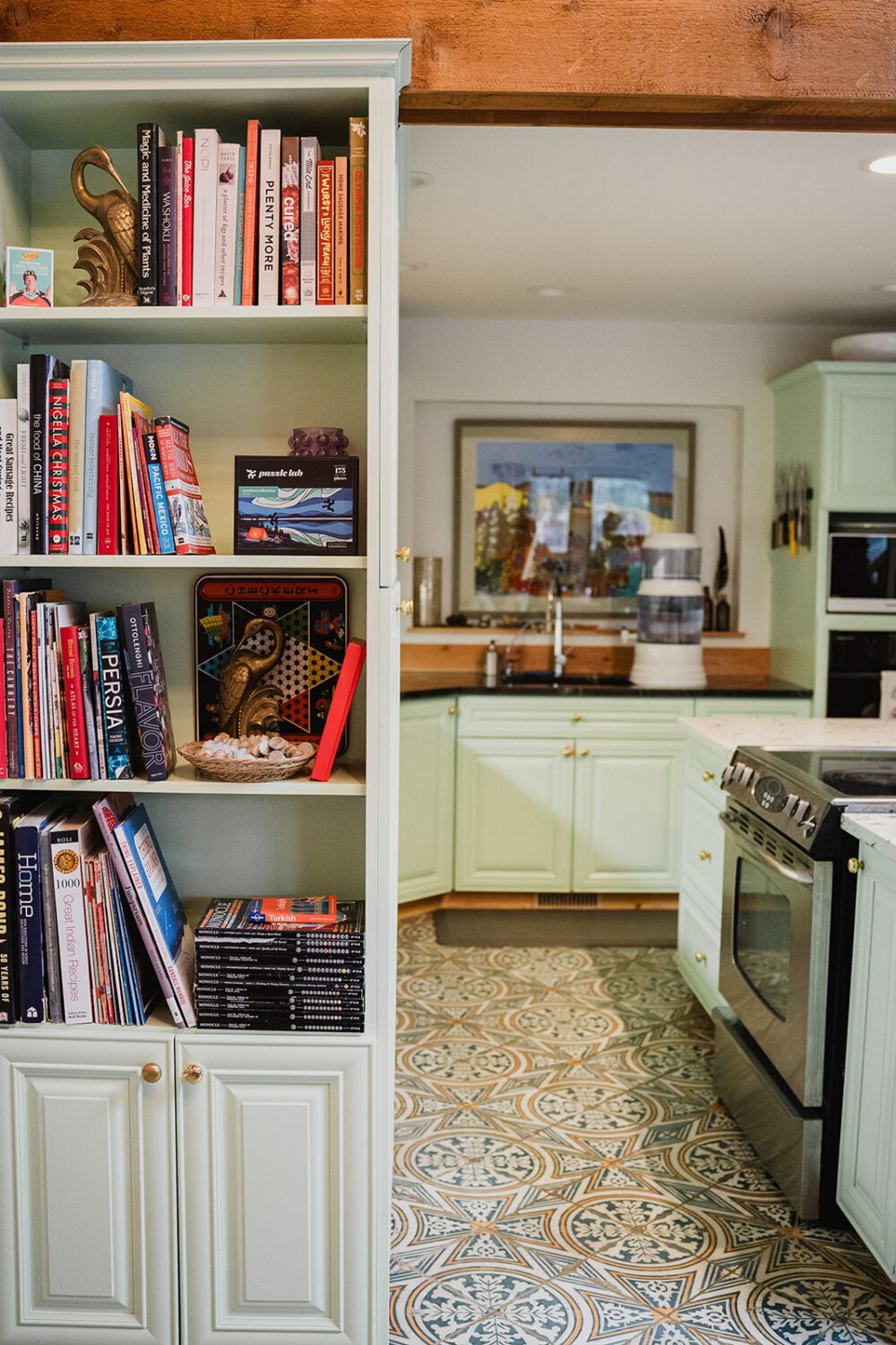 Built-in bookshelf filled with cookbooks and games beside a bright green kitchen inside The Spot lakeside retreat.