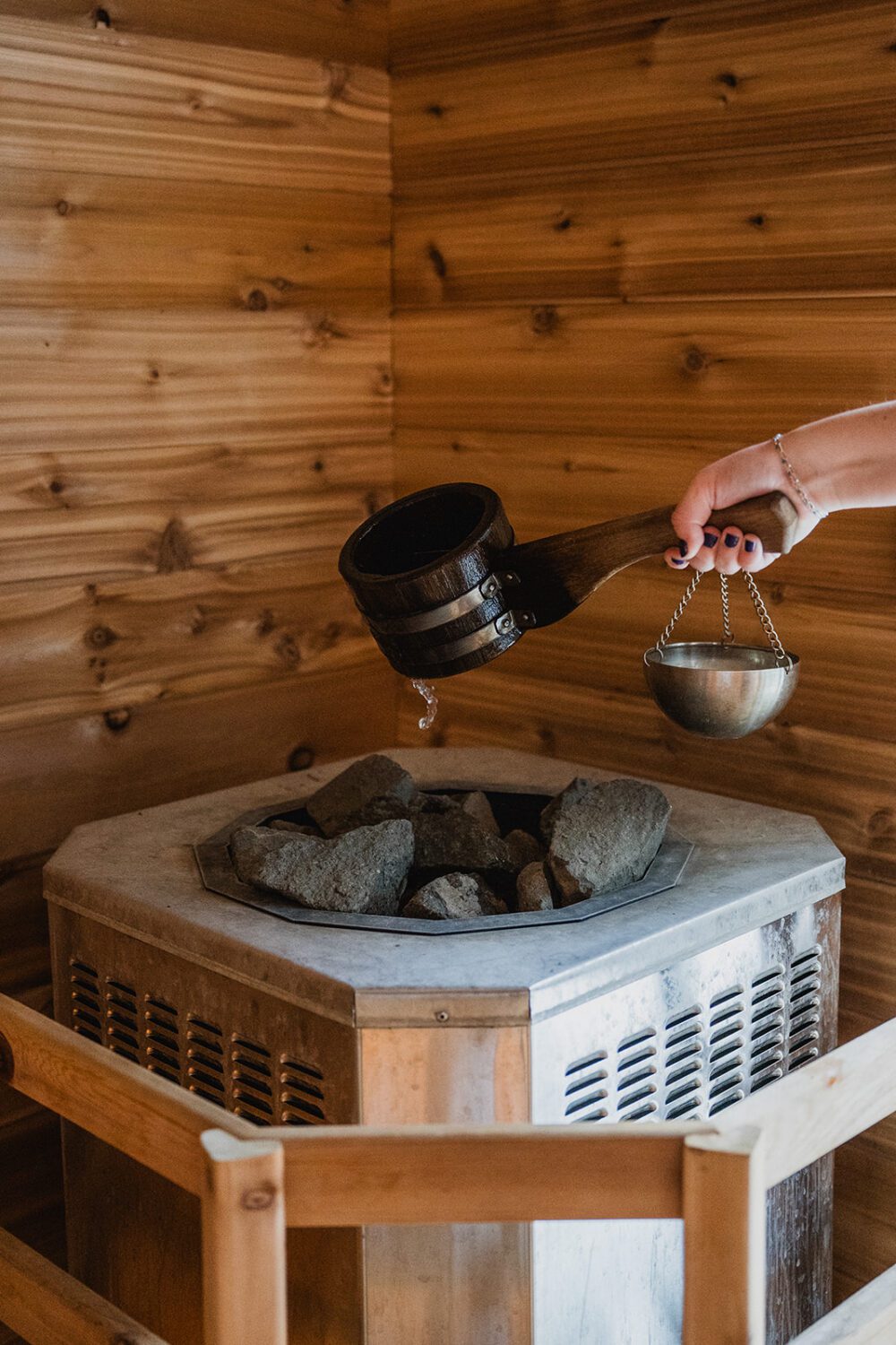 Water being poured over hot sauna rocks inside the wood-lined sauna at The Spot.
