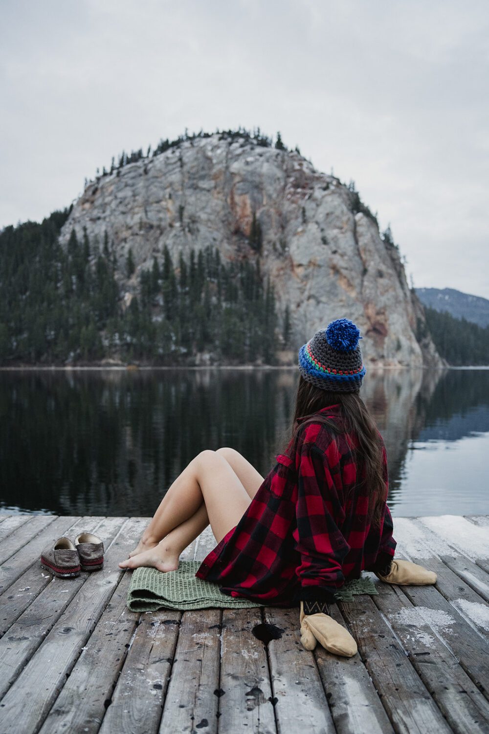 Woman sitting on the dock at Paul Lake after a cold plunge, wearing a red plaid shirt and knit toque.
