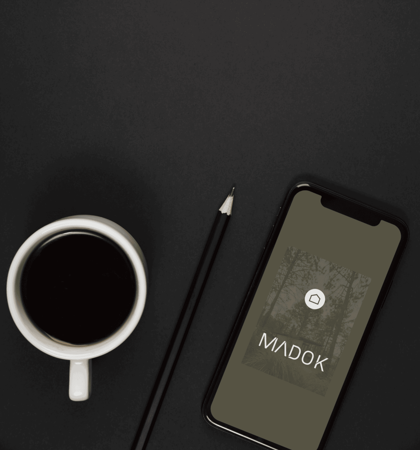 Smartphone displaying the Madok Developments visual identity and logo created by Pepper beside a coffee cup and pencil.